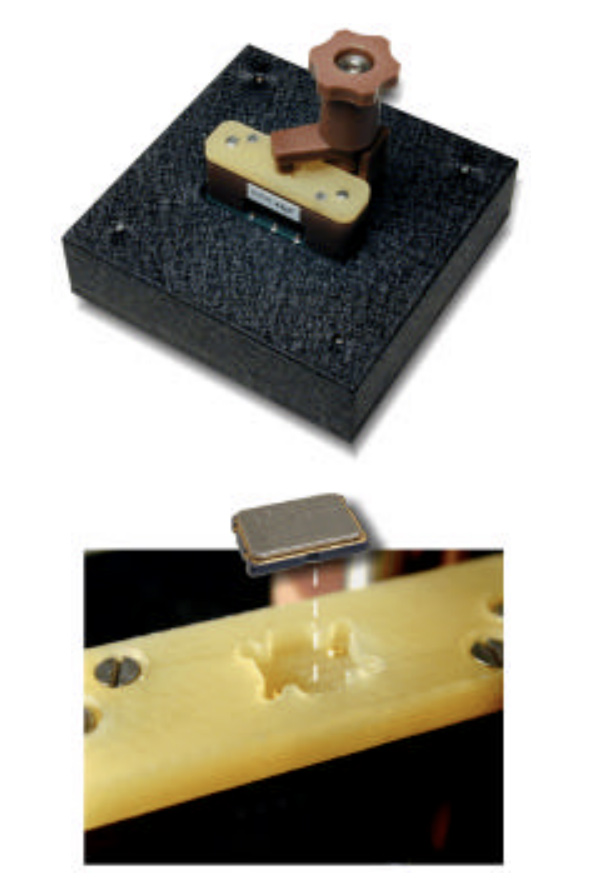 Piezo contact pickup being installed on a guitar neck: a small sensor placed into a routed slot on a wooden board with a mounting block and fasteners.